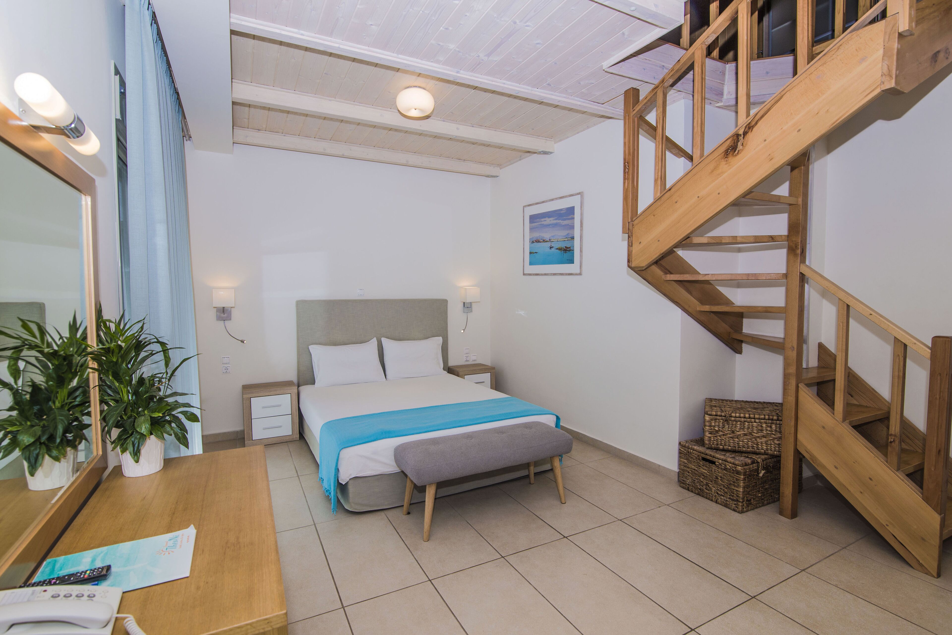 Quarto com cama, mesas de cabeceira, escrivaninha com uma planta, escada de madeira e um quadro na parede.