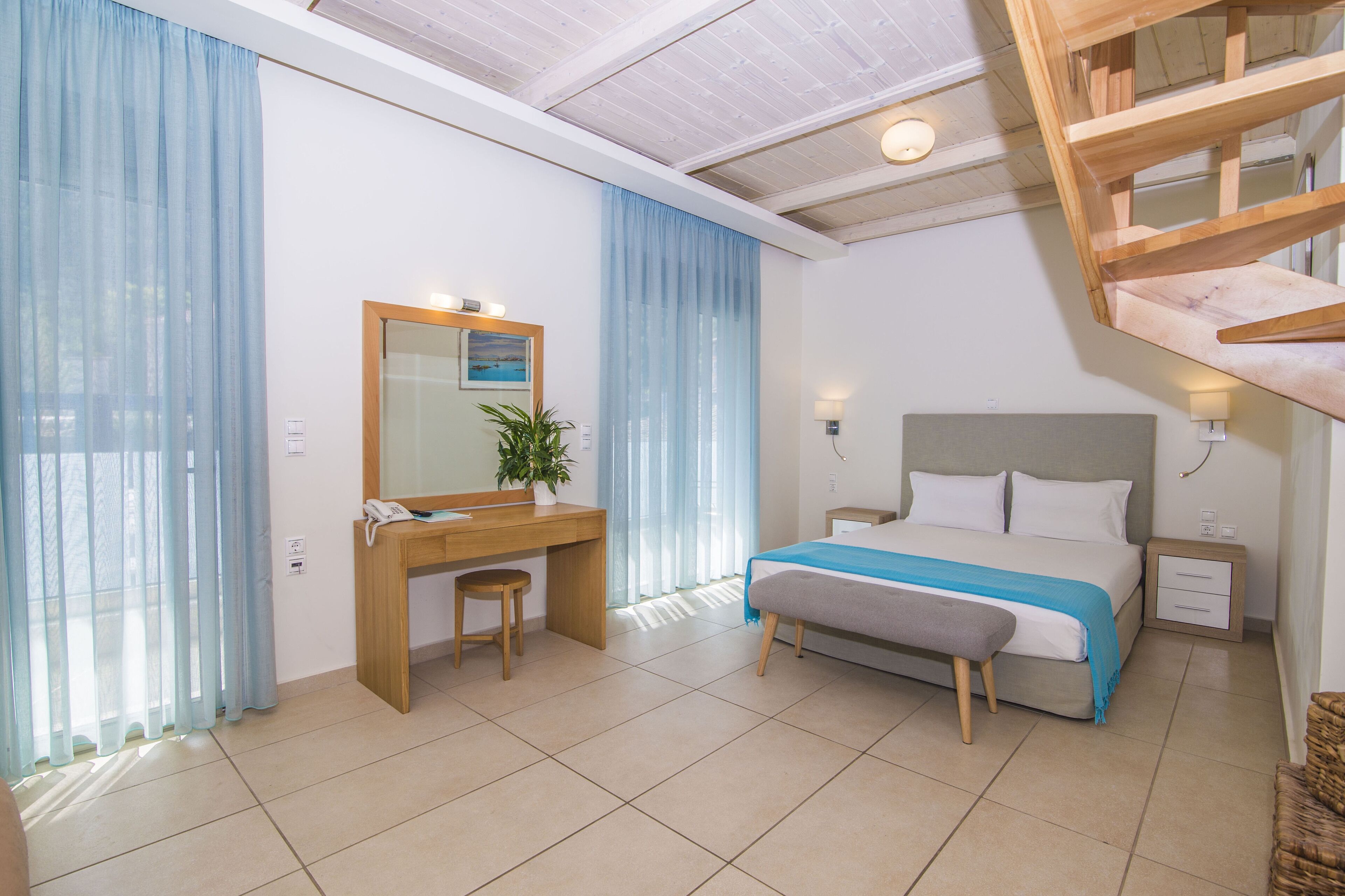 A bedroom with a bed, bedside table, desk, chair, and a wooden staircase.