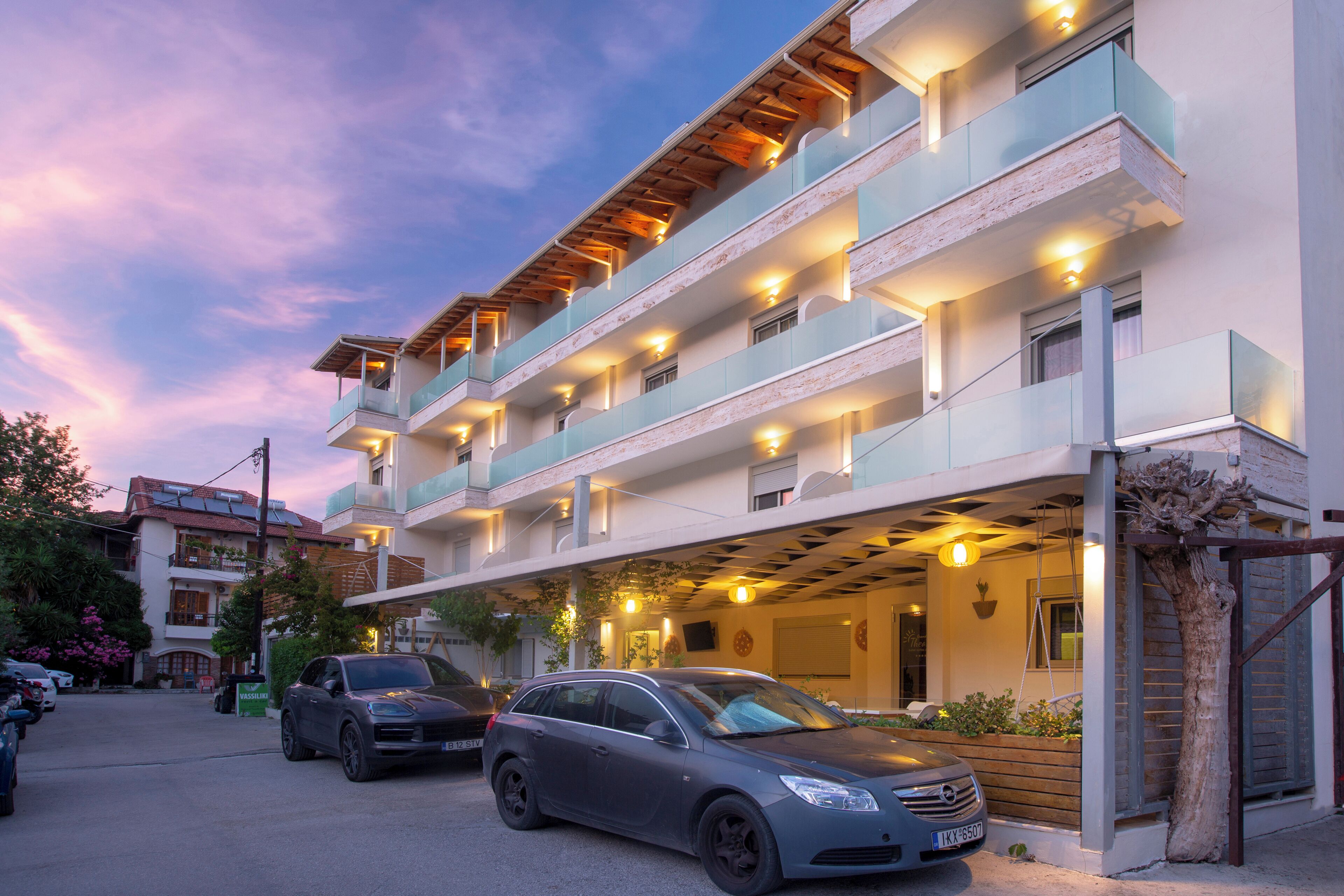 A multi-story hotel with balconies, a covered parking area, and a car parked in front.