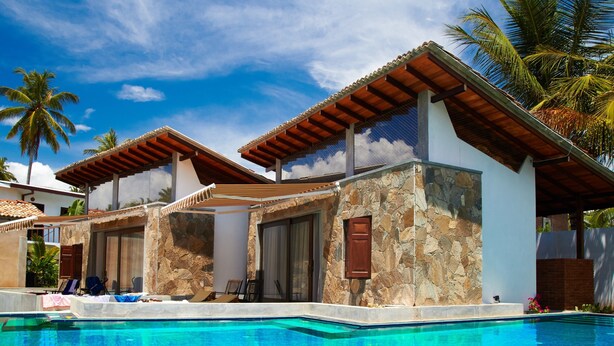 Un área junto a la piscina con una piscina azul cristalina, paredes de piedra y pérgolas de madera.