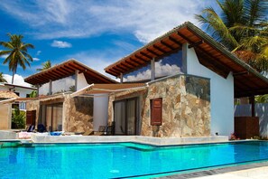 A poolside area with a clear blue pool, stone walls, and wooden pergolas. - Villa Tangalle Lagoon (Tangalle)