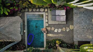 Vista aérea de una piscina rodeada de rocas y plantas, con una persona y un flotador azul.