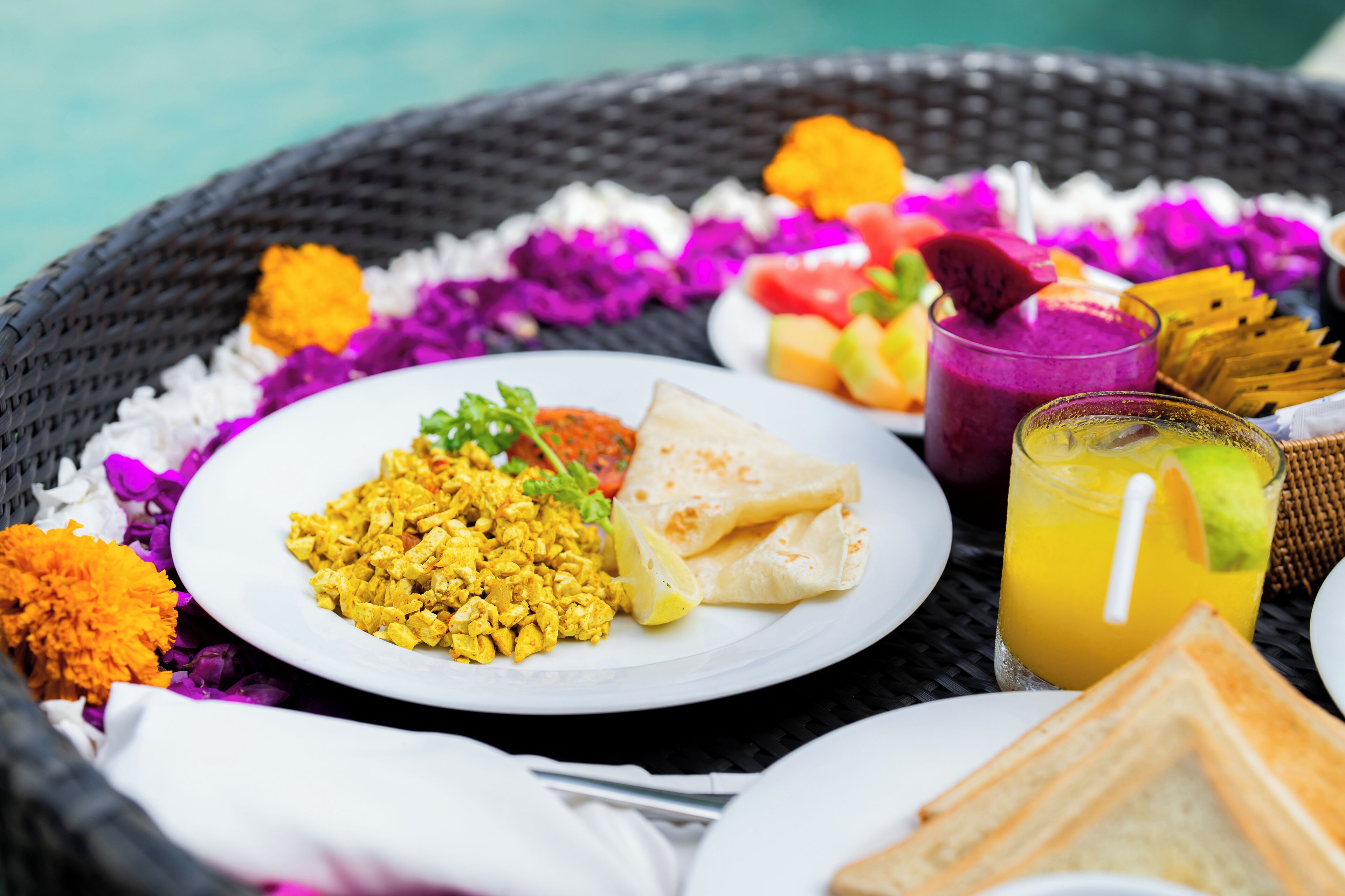 A wicker basket containing a plate of scrambled eggs, a slice of toast, a glass of orange juice, and a fruit salad.