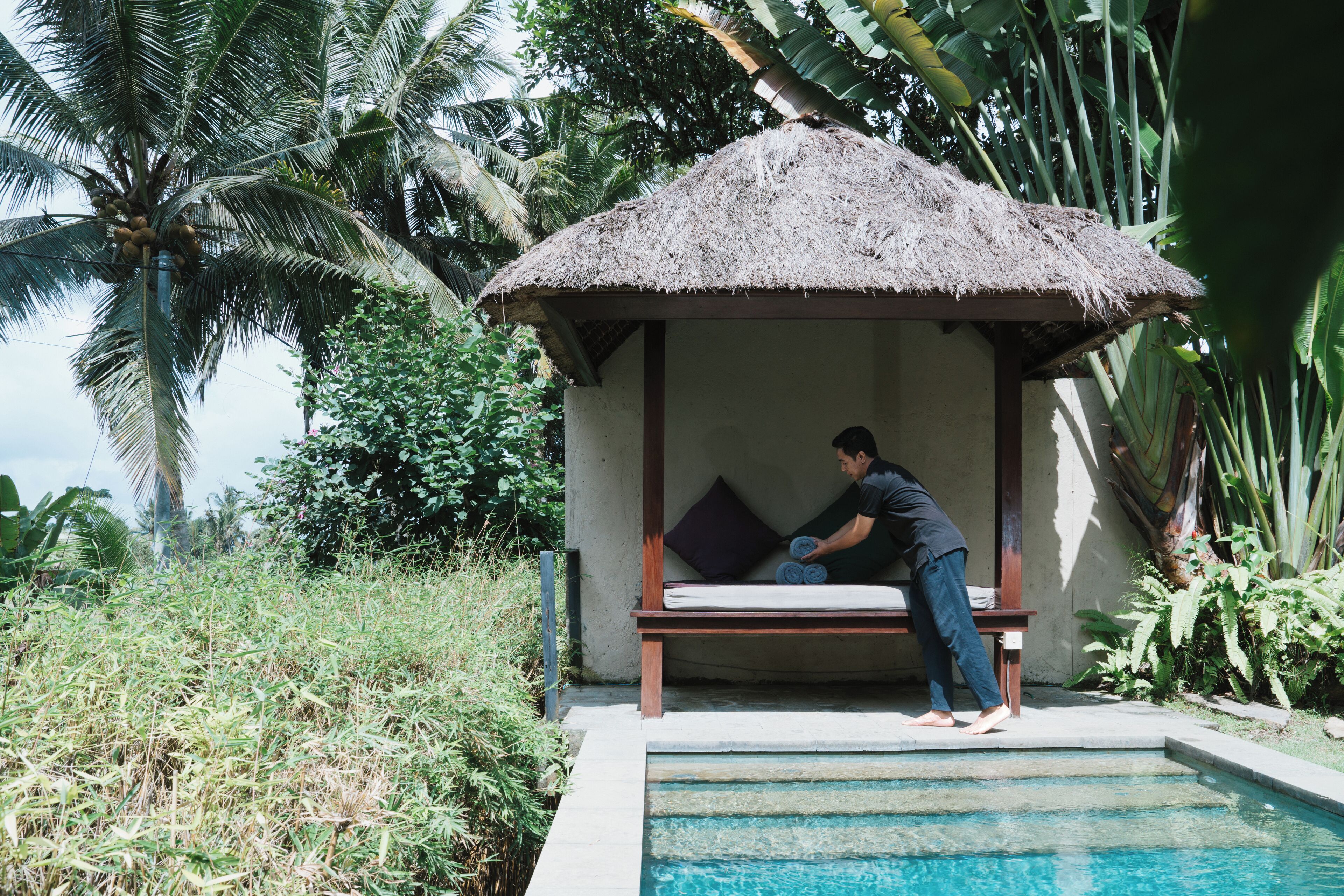 A thatched-roof hut with a bench and a pool.