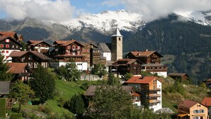 A mountain village with traditional wooden houses, a church tower, and snow-capped mountains in the background. - The Alpina Mountain Resort  (Tschiertschen)