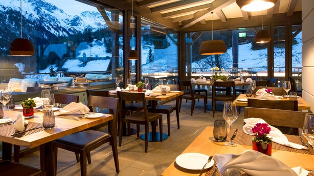 A restaurant with tables set for dining, large windows with a snowy mountain view, and pendant lighting. - The Alpina Mountain Resort  (Tschiertschen)