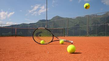 Una cancha de tenis con red, pelotas y una raqueta.