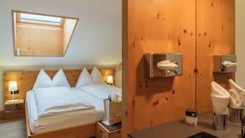 Une chambre à coucher avec une tête de lit en bois, un puits de lumière, un lit avec du linge de lit blanc, des lampes de chevet, une table de chevet en bois et une salle de bain avec un mur en bois, un lavabo et des distributeurs de serviettes.