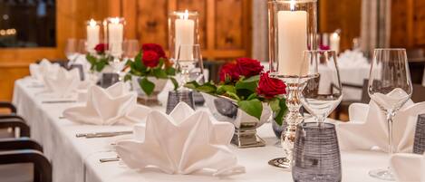 A dining table set with white tablecloths, candles, red roses, and clear glassware.