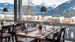 A restaurant with wooden tables and chairs, set against a backdrop of snow-capped mountains. - The Alpina Mountain Resort  (Tschiertschen)