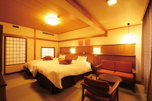 Habitación de hotel de estilo japonés tradicional con suelo de tatami, una cama grande con almohadas, una mesita baja y un banco acolchado rojo.