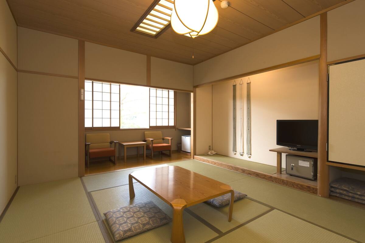 A traditional Japanese room with tatami flooring, a low table, seating, a television, and sliding doors.