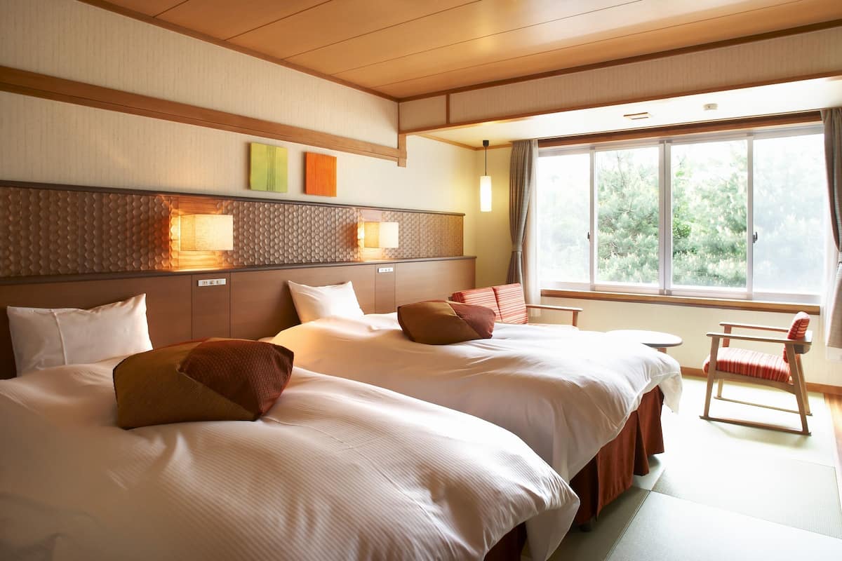 A hotel room with two beds, a window with curtains, and a wooden chair.
