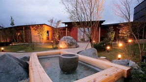 A traditional Japanese onsen with a wooden bath surrounded by rocks and a stone basin in the center. - Satoyama no Kyujitsu Kyoto Keburikawa (Kameoka)