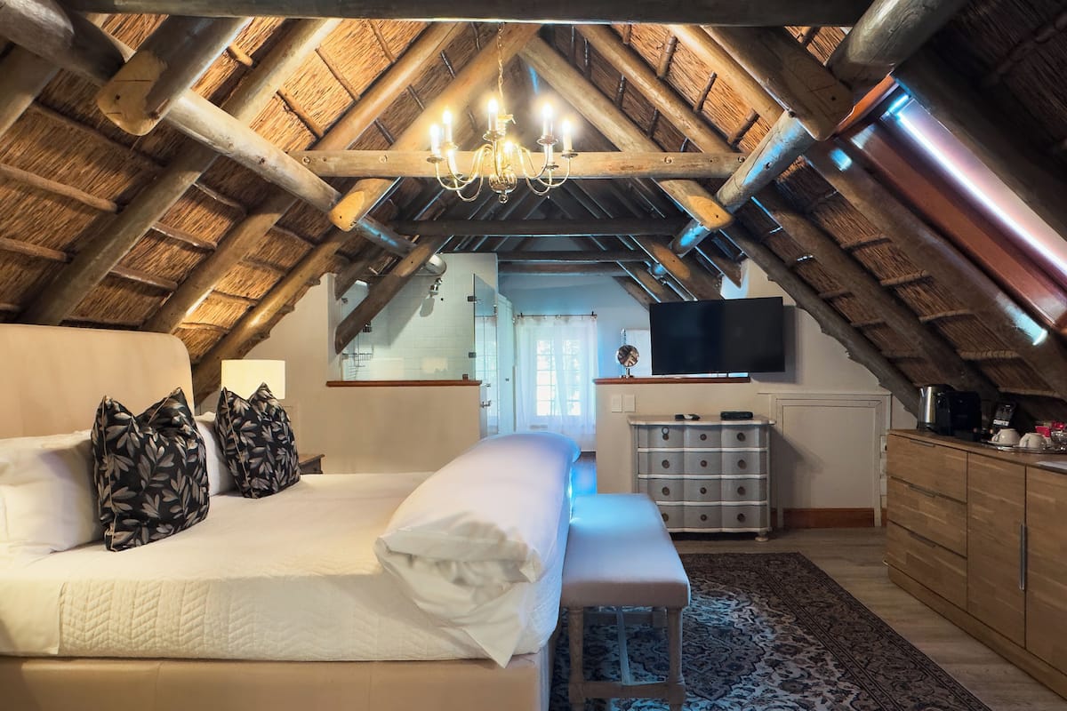 Ein Schlafzimmer mit hohen Decken, Holzboden, einem Bett, einer Bank, einem Schminktisch und einem Fernseher.