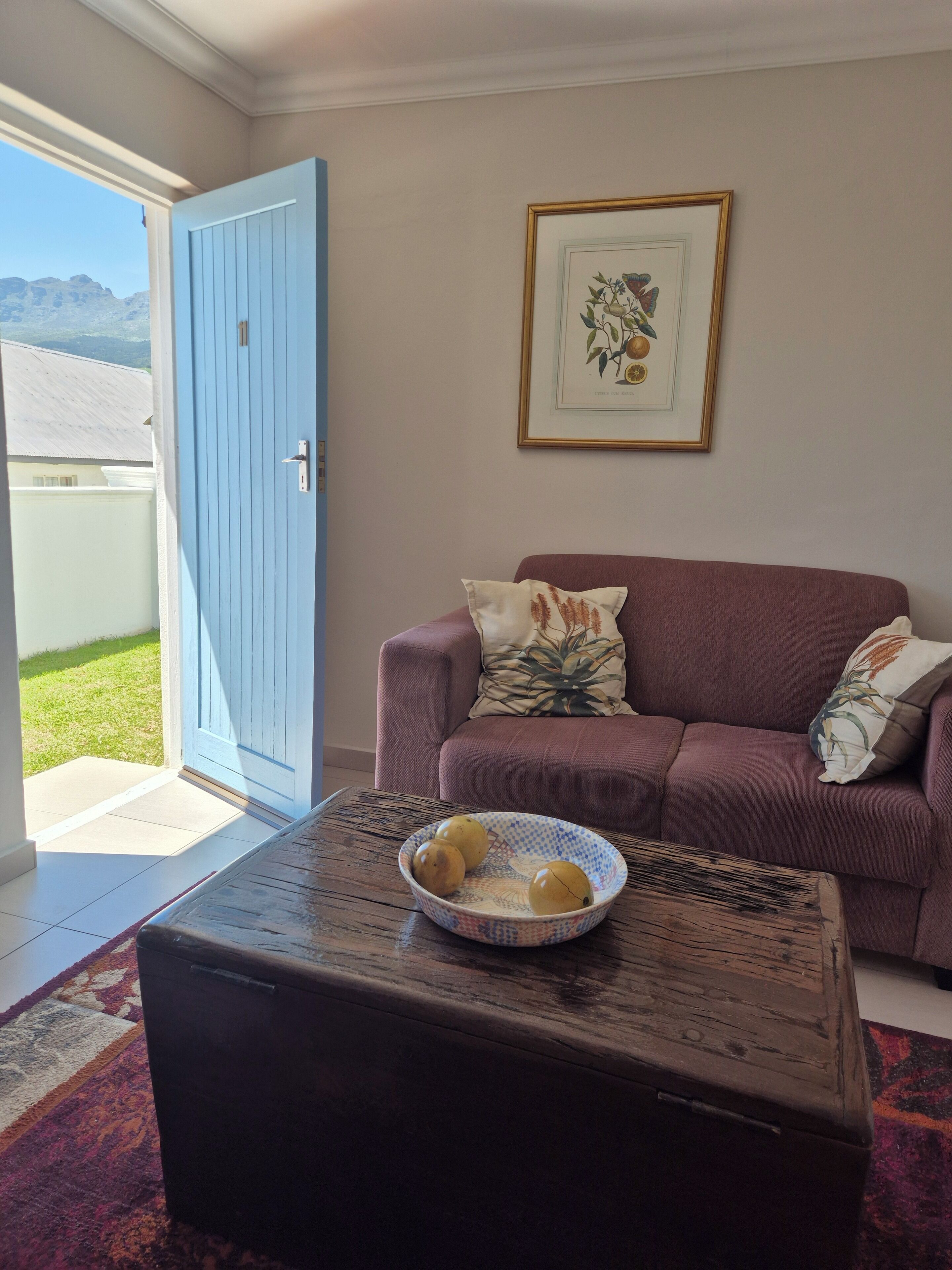A living room with a blue door, a purple sofa, and a coffee table with a bowl of fruit.