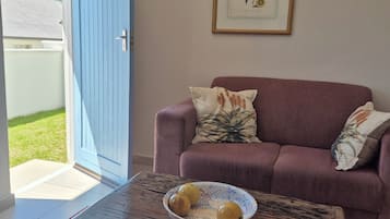 A living room with a blue door, a purple sofa, and a coffee table with a bowl of fruit.