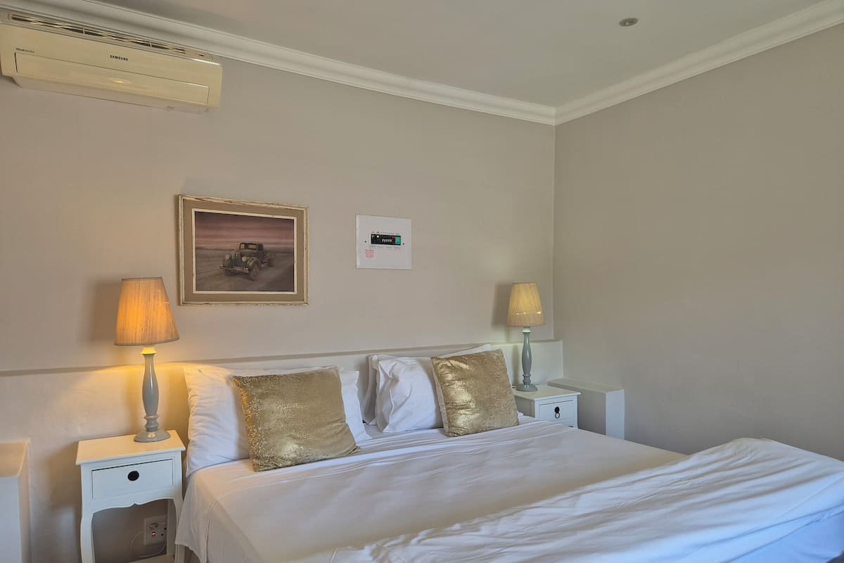 Ein Hotelzimmer mit einem Bett, zwei Nachttischen mit Lampen, einer Wand-Klimaanlage, einem gerahmten Bild und einem Thermostat.