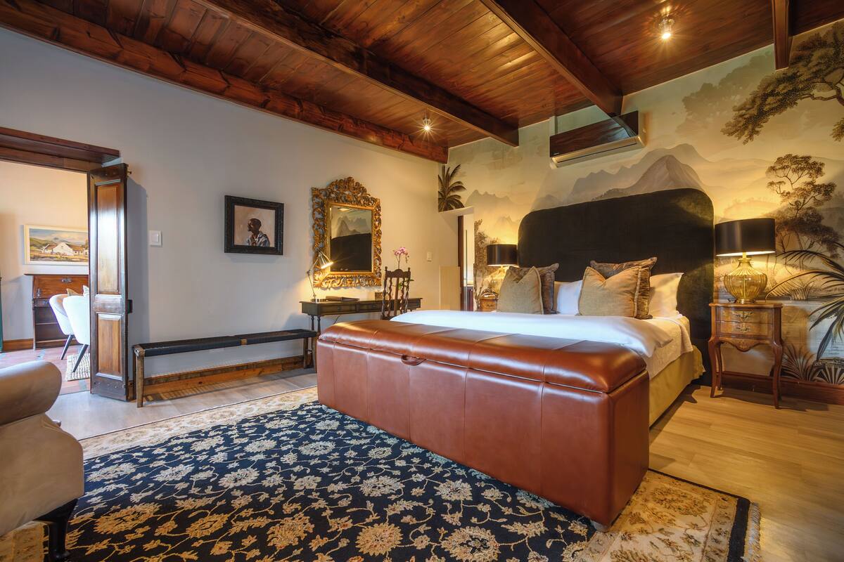 Ein Schlafzimmer mit einem großen Bett, einem Holzkopfende, einem Nachttisch, einer Lampe und einem Wandbild.