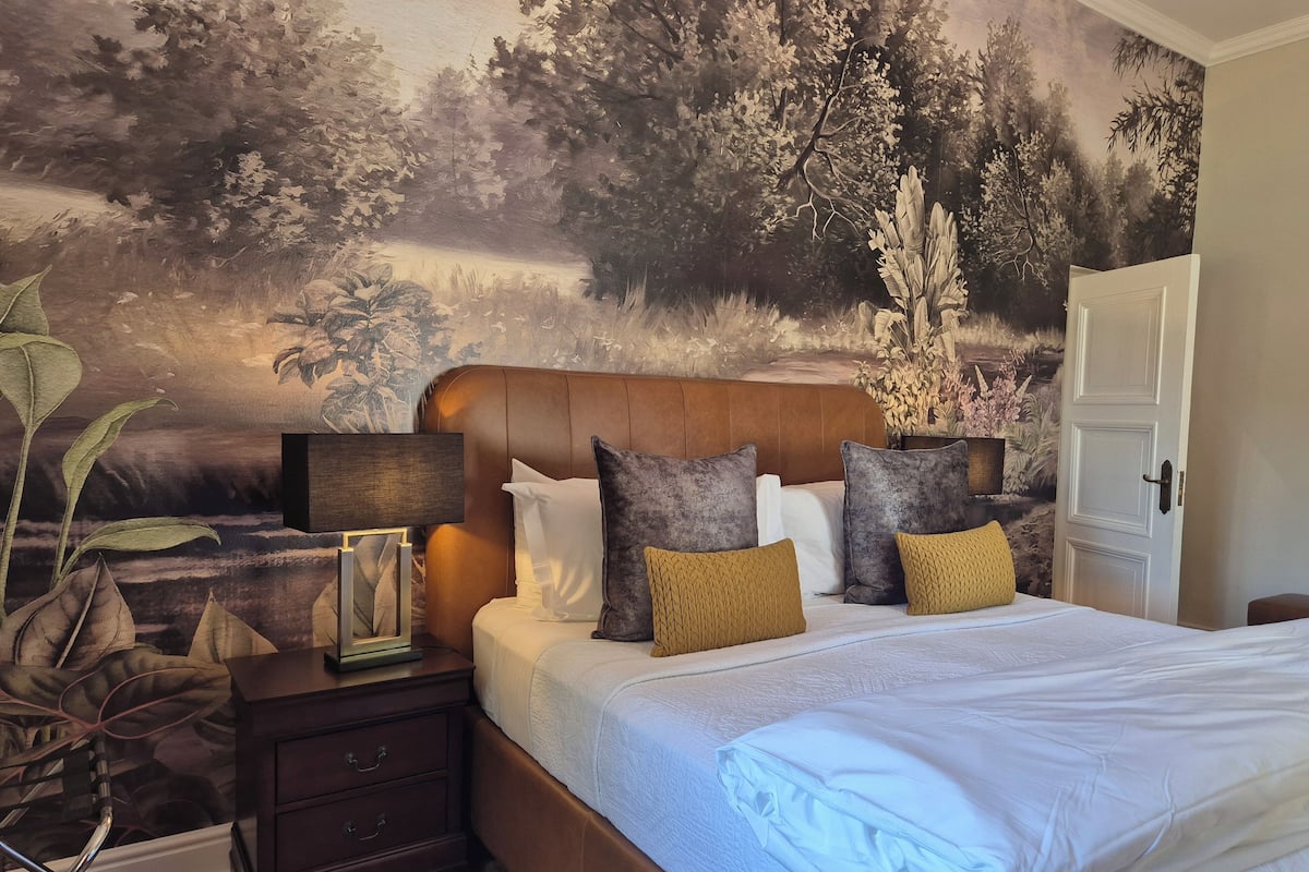 Ein Schlafzimmer mit einem großen Bett, einem Nachttisch mit Lampe und einer Wandmalerei von einem Wald.
