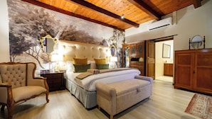 Een slaapkamer met een bed, een stoel, een bank, een houten kast en een plafond met houten balken.