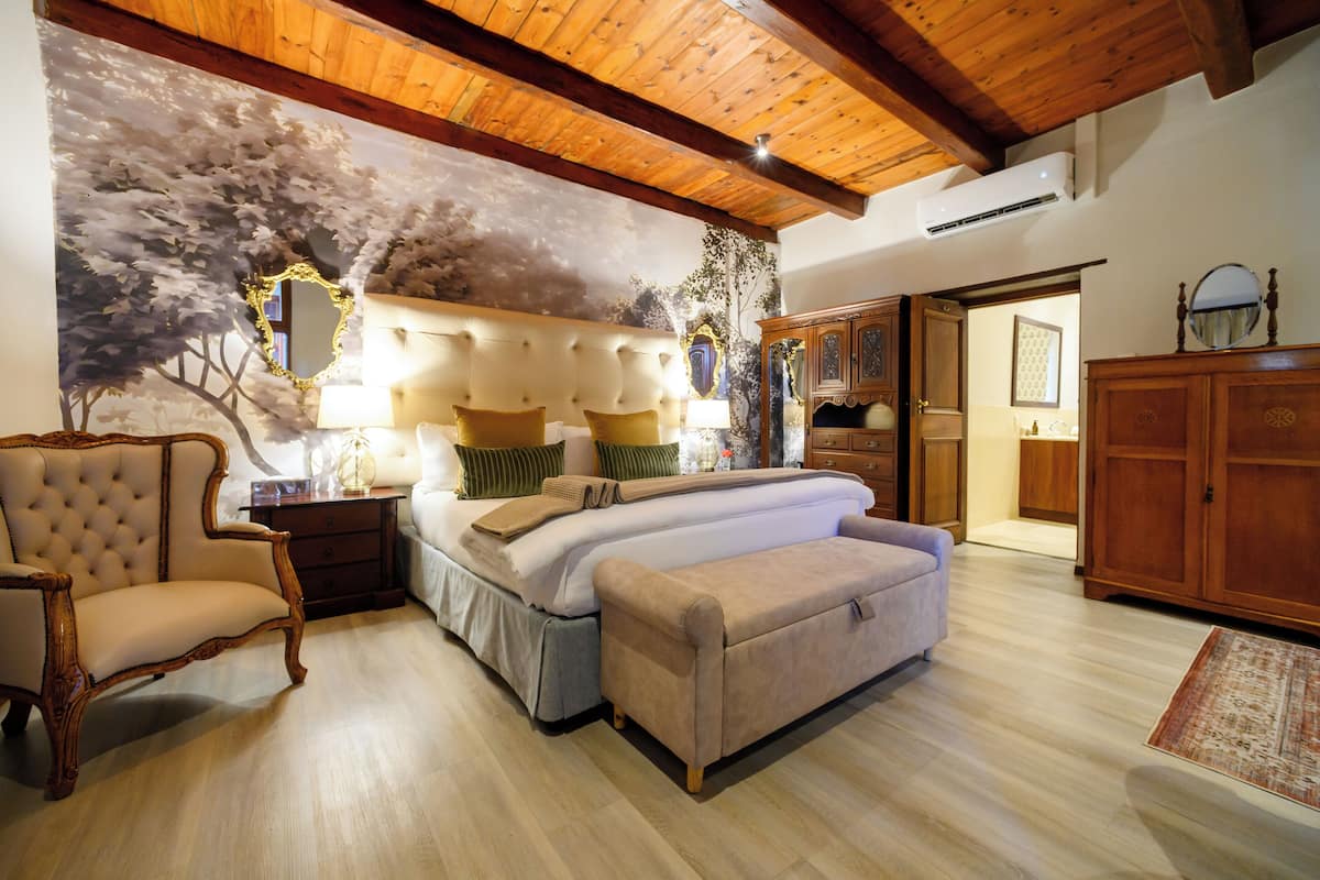 Ein Schlafzimmer mit einem Bett, einem Sessel, einer Couch, einem Holzschrank und einer Decke mit Holzbalken.