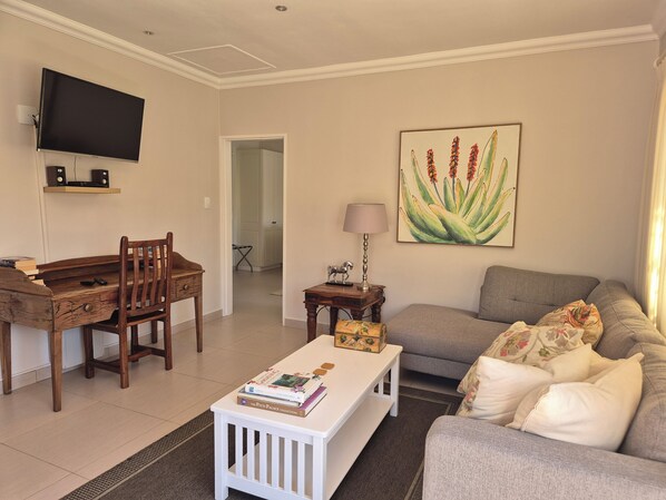 A living room with a wooden dining table, a white coffee table, a grey sofa, and a television mounted on the wall.