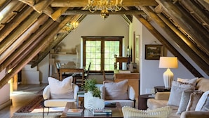 Een zolderkamer met zichtbare houten balken, een kroonluchter en een gezellige zithoek met banken en een salontafel.