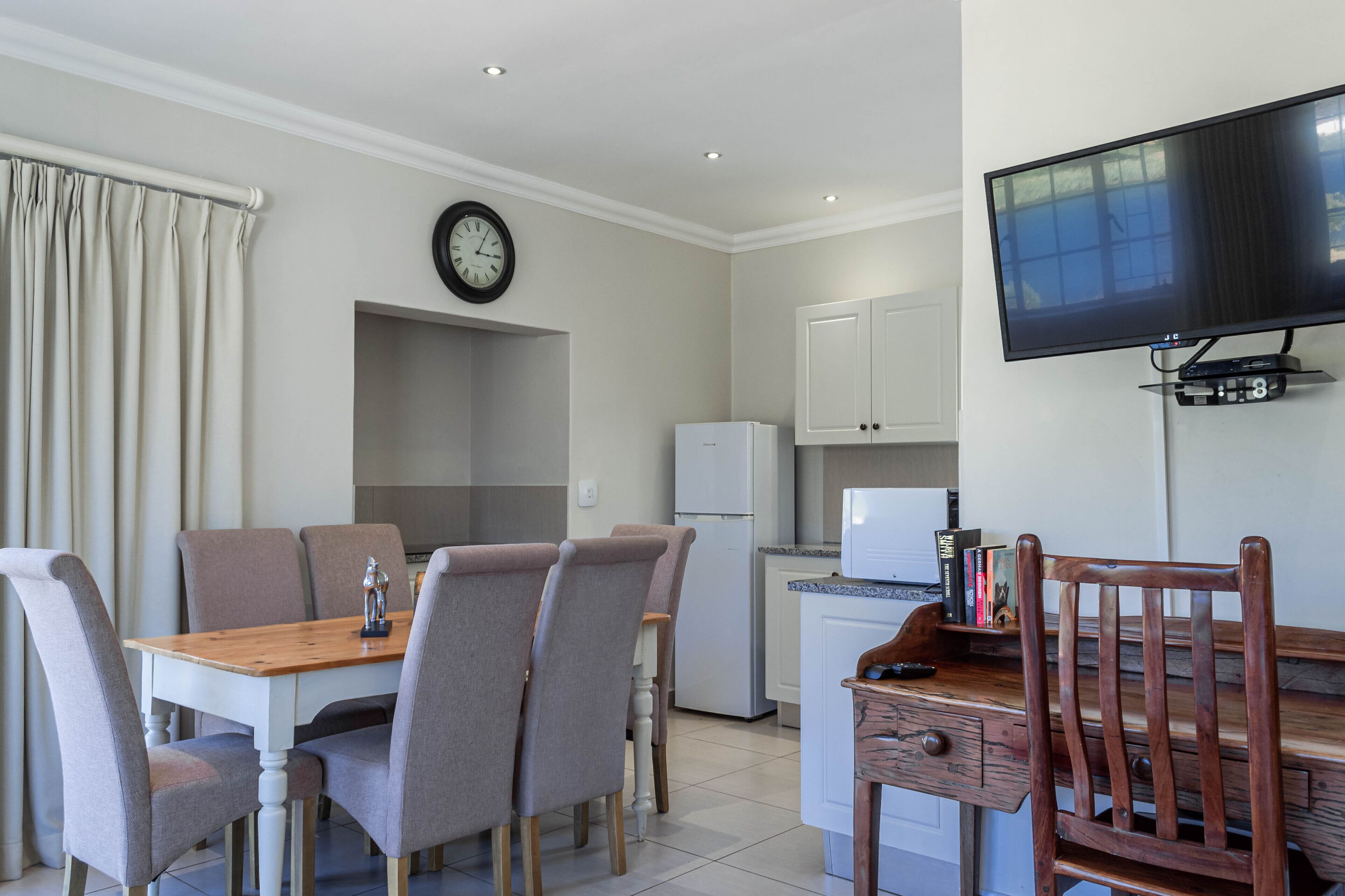 Una cocina moderna con comedor, un televisor de pantalla plana en la pared y un reloj también en la pared.