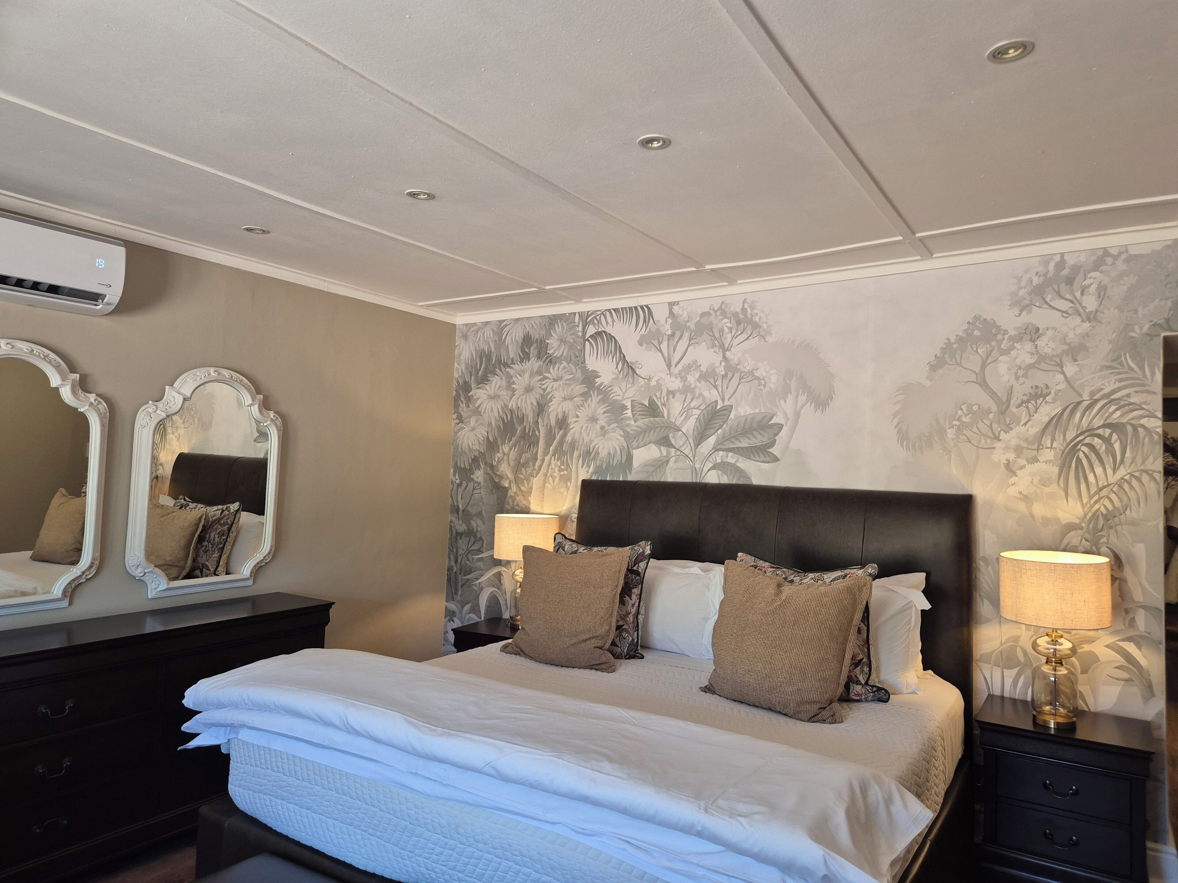 A hotel room with a large bed, two bedside tables with lamps, a dark headboard, and a floral wallpaper.