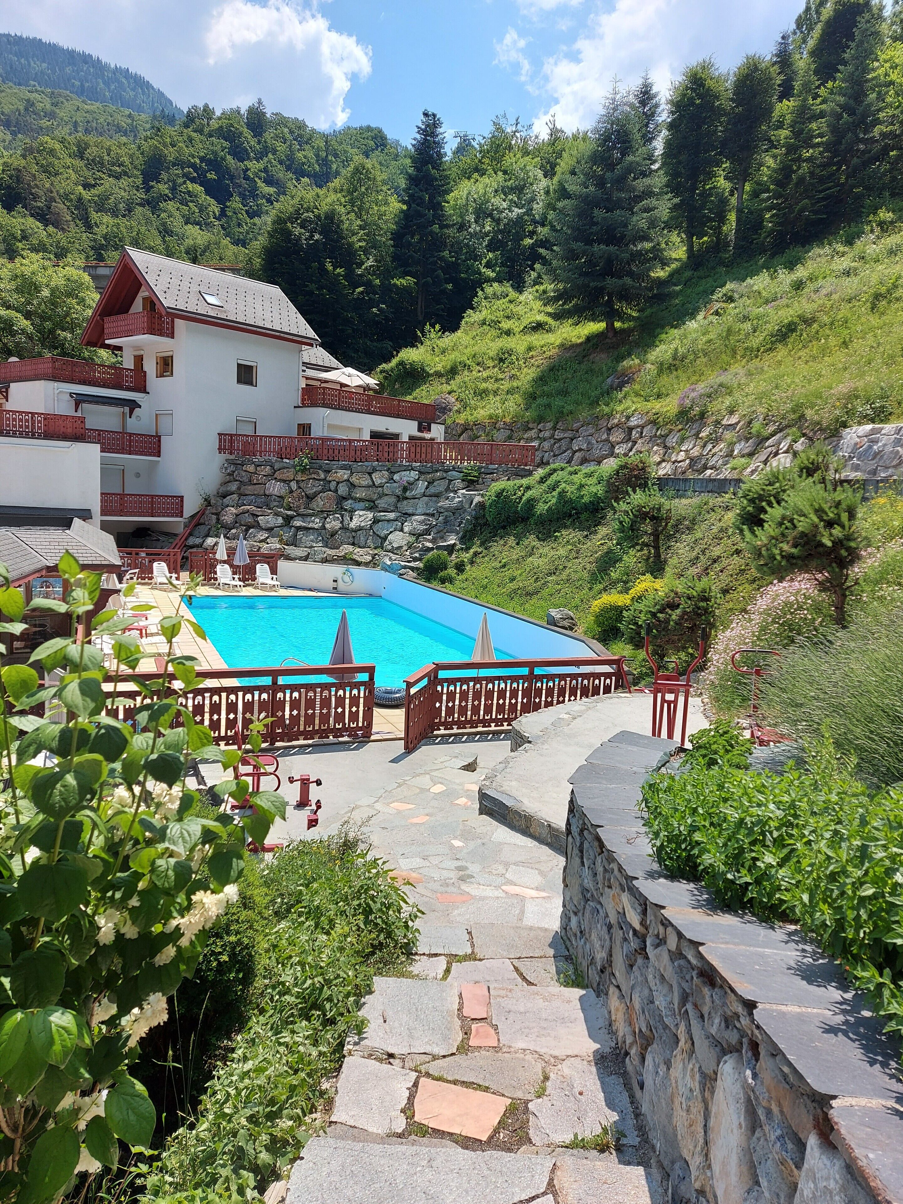 A resort with a swimming pool, stone steps, and a view of a forested hillside.