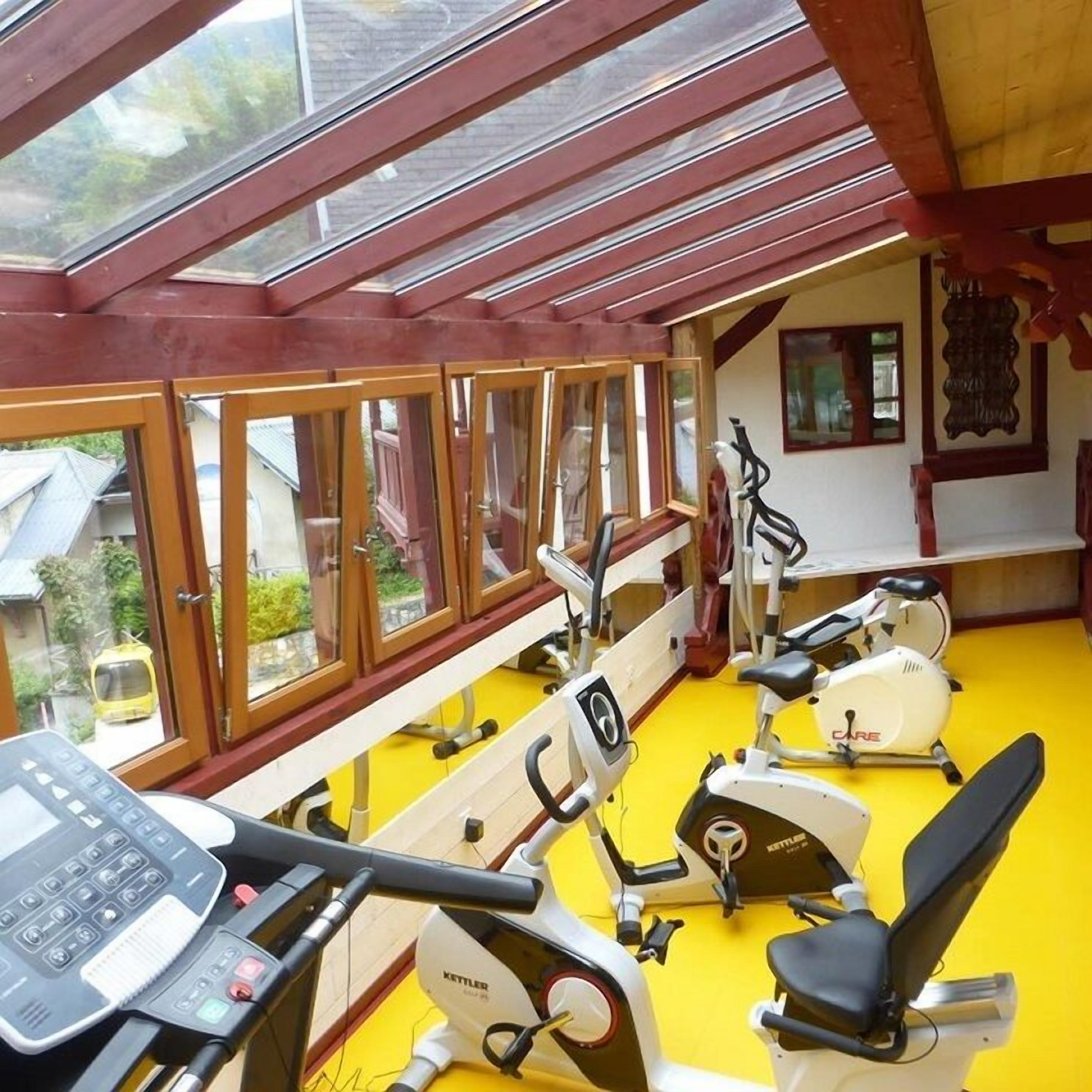 Ein Fitnessstudio mit Trainingsgeräten, großen Fenstern und einem gelben Boden.