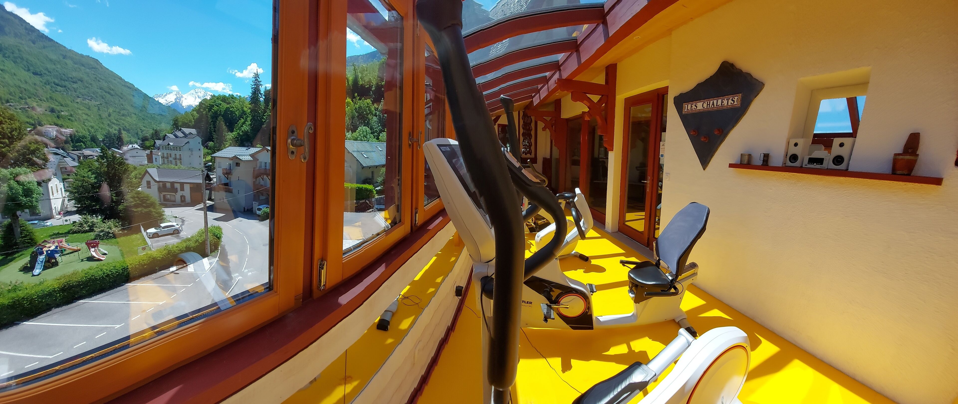 Habitación con vistas a un pueblo y montañas, una caminadora y un cartel que dice 'LES CHALETS'.