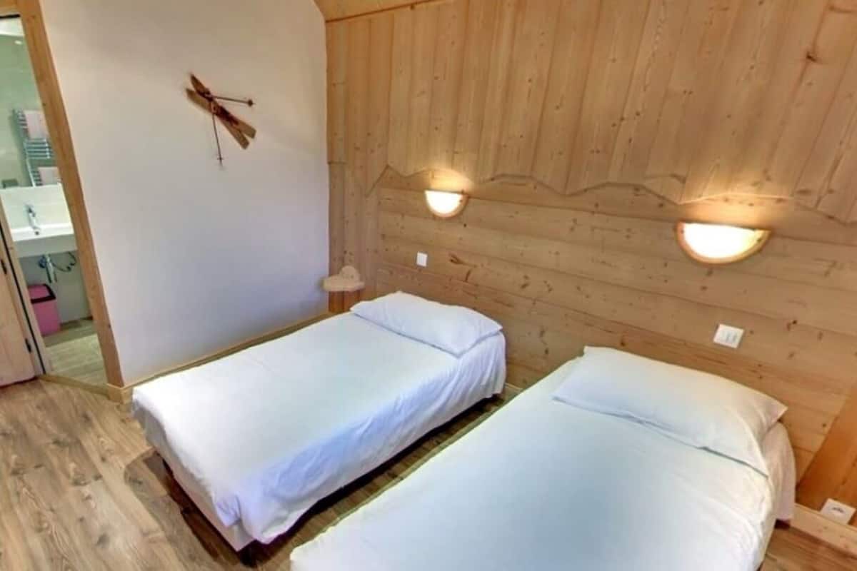 Une chambre avec deux lits simples, des murs en bois et deux lampes fixées au mur.