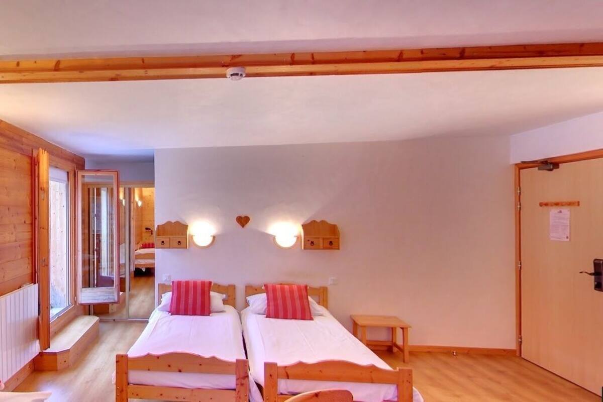 Une cabane en bois avec deux lits simples, un banc et une porte sur laquelle est affiché un avis.