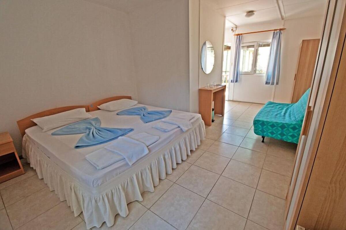 A hotel room with a large bed, a smaller bed, a bedside table, a mirror, and a window with curtains.