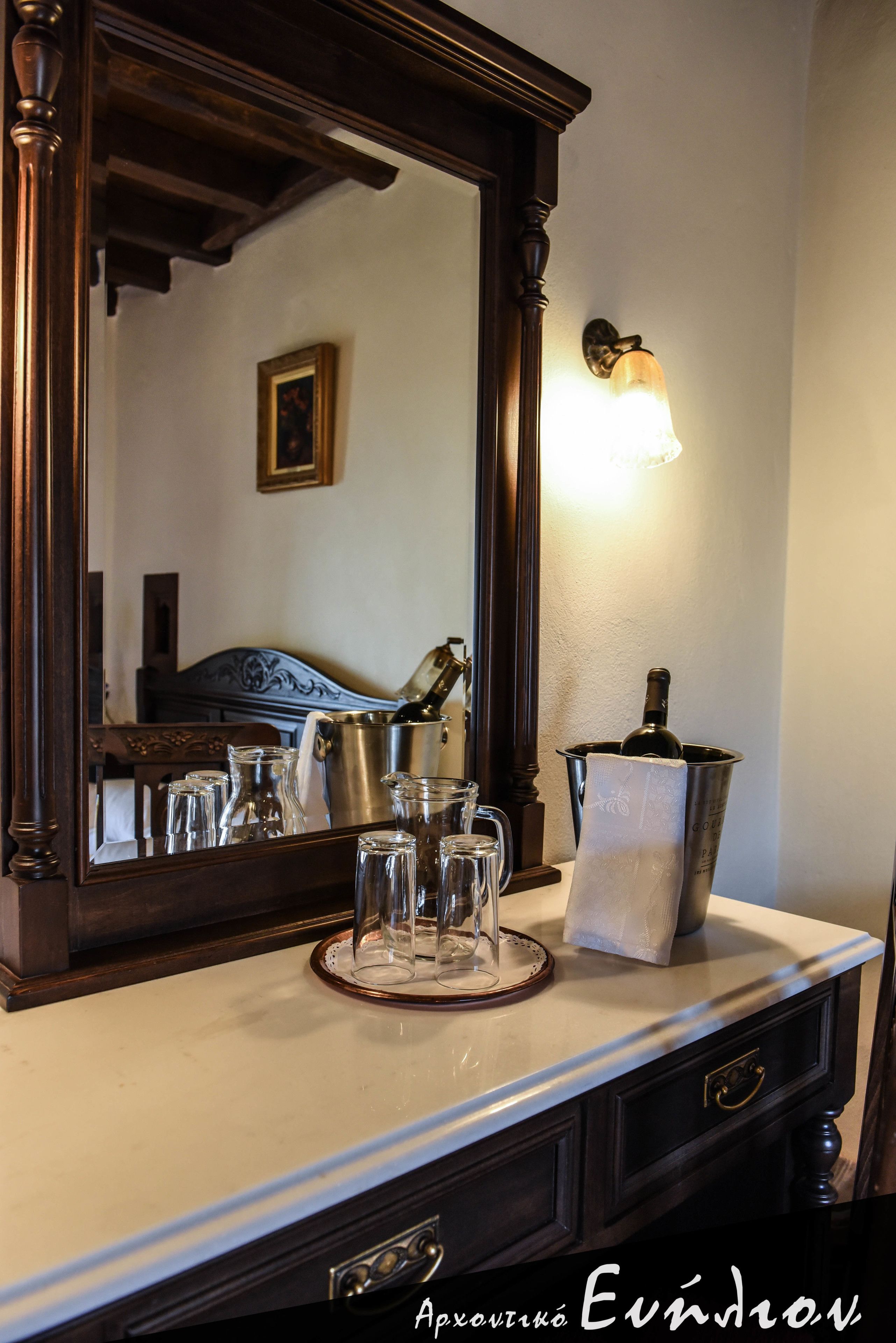 A hotel room with a large mirror, a bedside table with a wine bottle, glasses, and a pitcher.