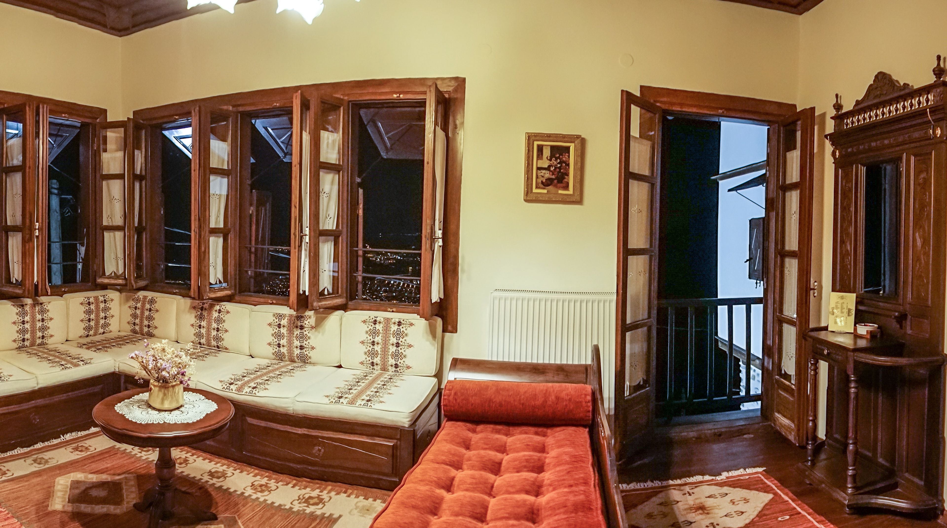 A traditional room with a sofa set, a small table, and a red ottoman. There is a radiator on the wall and a wooden cabinet.