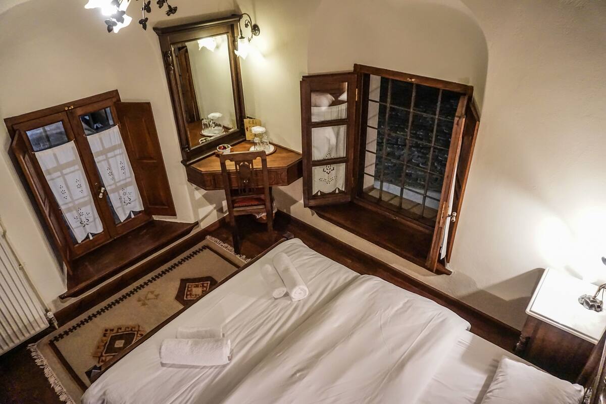 Una habitación de hotel con cama, escritorio de madera, espejo y ventana con vistas.