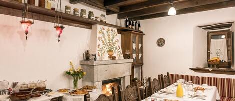 Un espace repas avec une longue table dressée pour le repas, des poutres en bois au plafond et une cheminée.