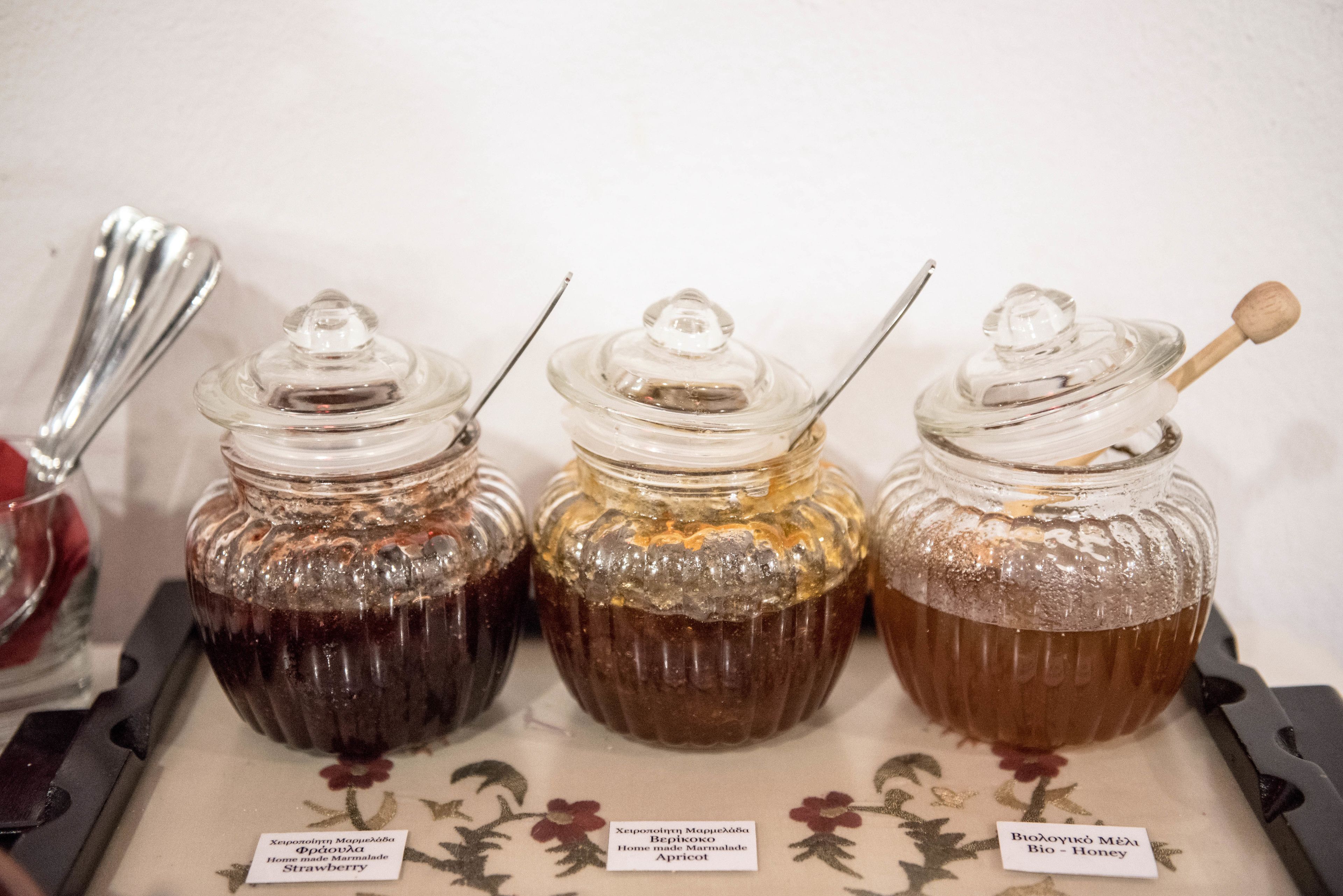Three glass jars with metal lids, each containing a different type of honey, labeled in a foreign language.