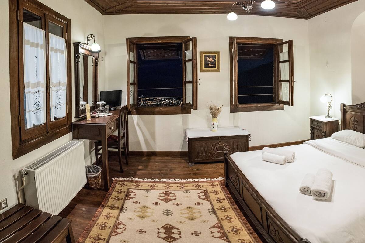 Un dormitorio tradicional con una cama grande, muebles de madera y vistas a través de una ventana abierta.