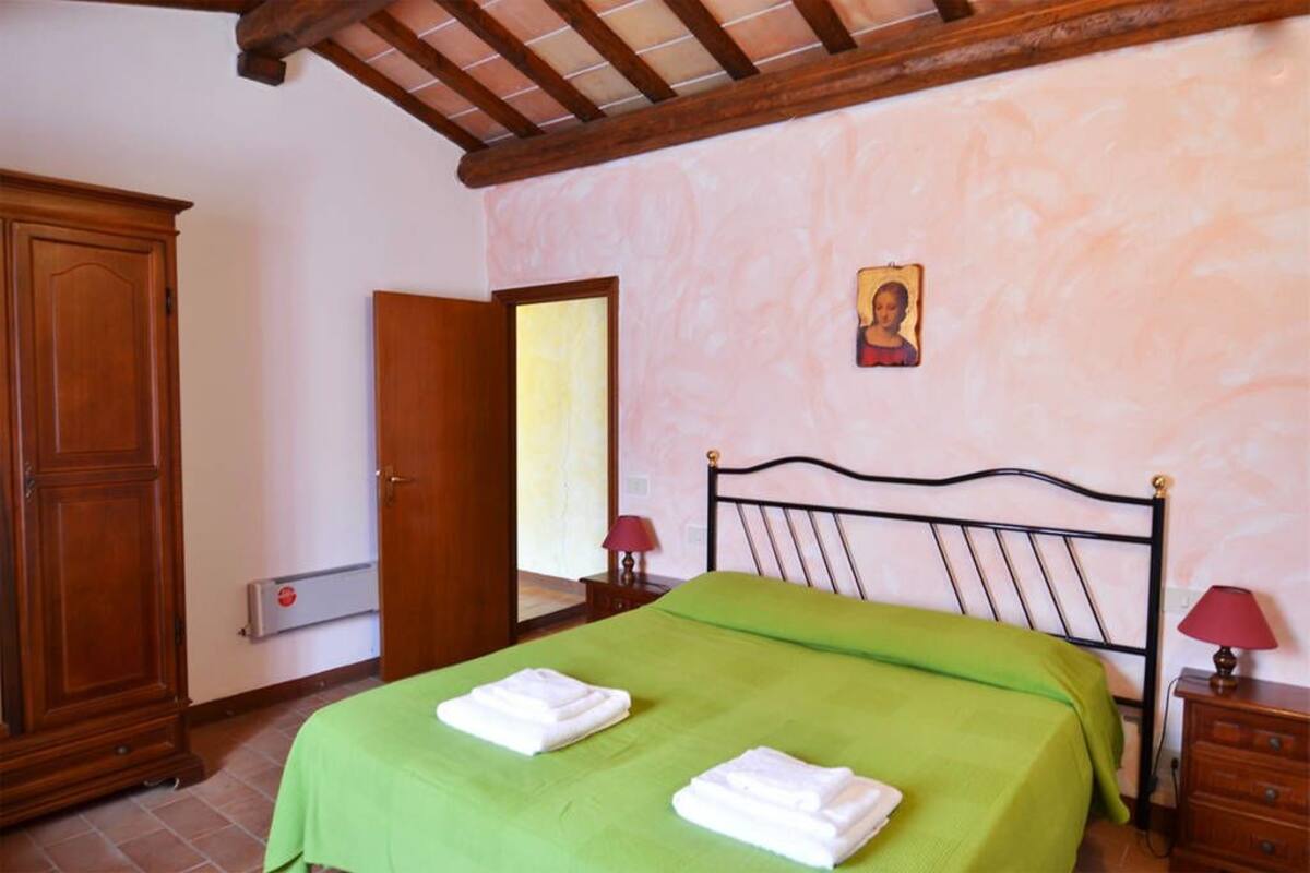Un dormitori amb un llit, un armari de fusta, una nitòria amb una làmpada i una fotografia penjada a la paret.