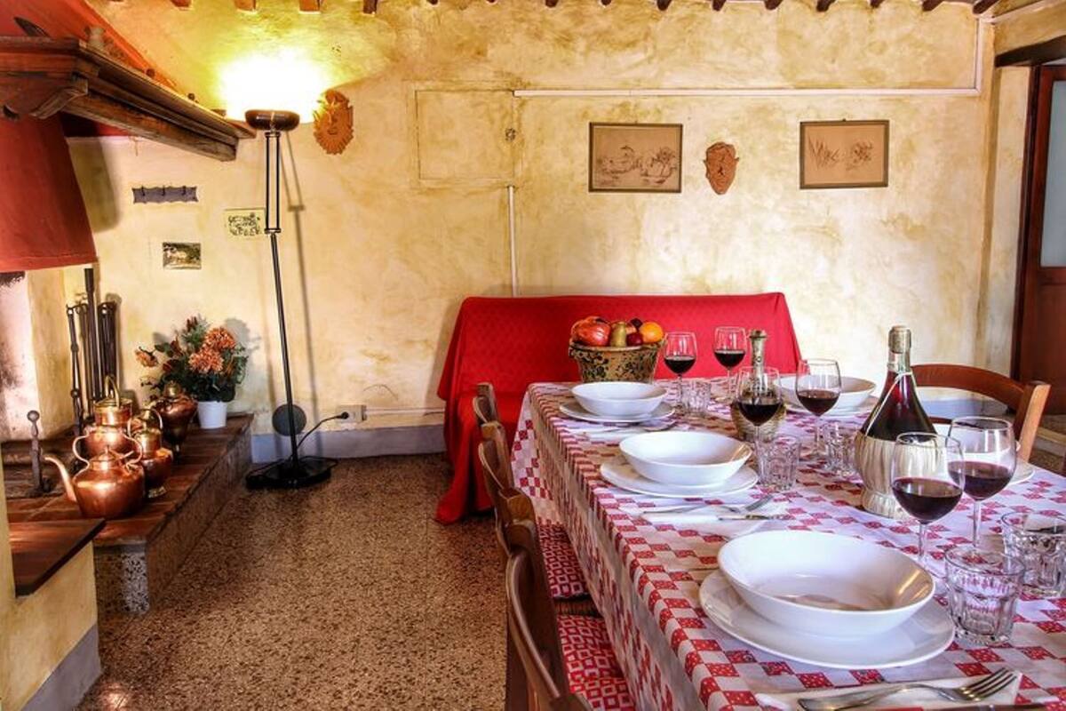 Zona de menjador amb una taula preparada per a quatre, amb un mantell vermell, plats blancs i copes de vi. Hi ha olles de coure sobre una prestatgeria a l'esquerra i un teixit vermell drapat per l'esquena de la taula.