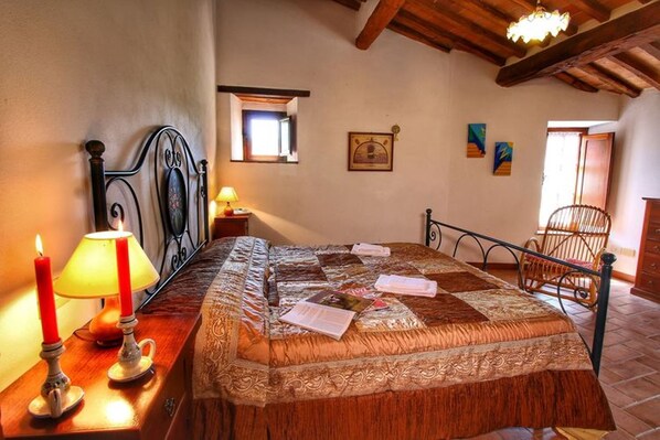 Un dormitorio con cama, mesita de noche con lámpara, una silla y una ventana.