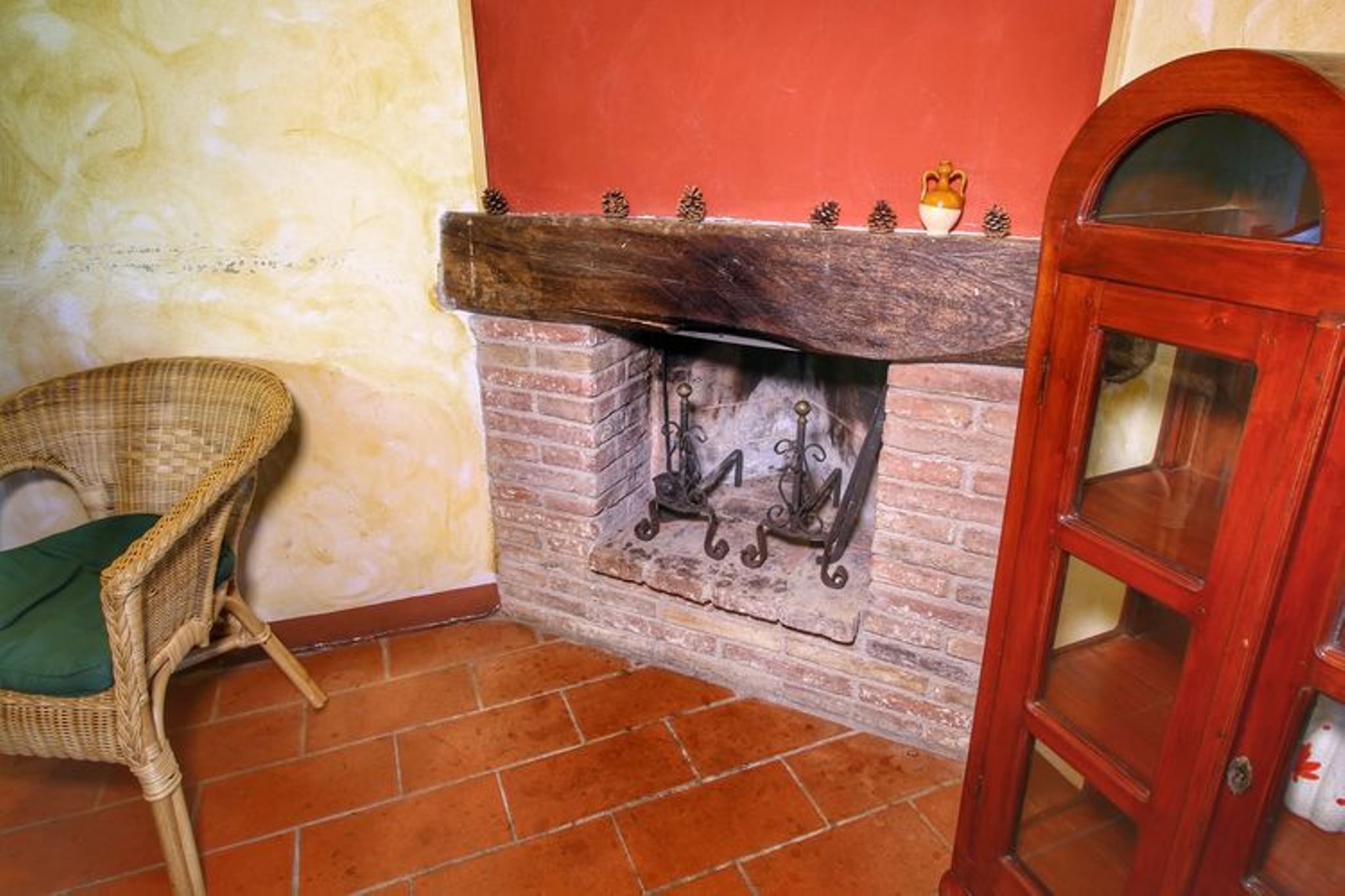 Quarto nos fundos com lareira de tijolos, uma cadeira de vime e um armário de madeira.