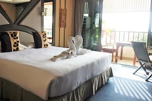 A hotel room with a neatly made bed, a balcony with a chair, and a view of the outdoors.
