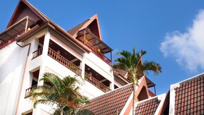 A multi-story building with balconies, red-tiled roofs, and palm trees. - Kelly’s Residency (Patong)