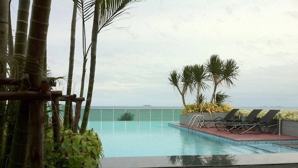 Ein Pool mit Blick auf den Ozean, umgeben von Palmen und Liegestühlen.