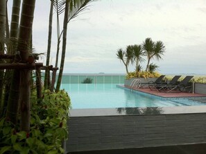 A pool with a view of the ocean, surrounded by palm trees and lounge chairs. - Thanyalak at The Gallery Condominium (Pattaya)